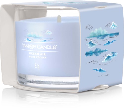 Et lys i en eske med hav- og sky-mønster, merket "Yankee Candle Ocean Air," med en hvit veke.