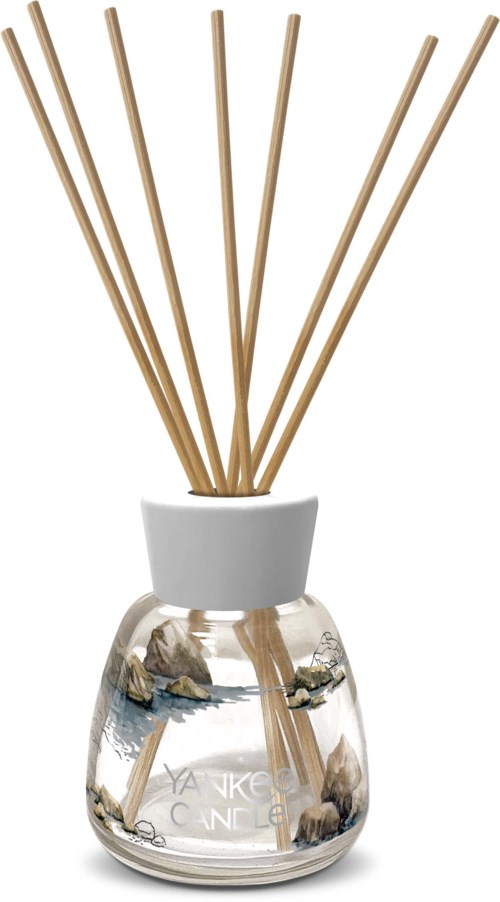 Een diffuser met houten stokjes in een doorzichtige glazen container gevuld met water en decoratieve stenen.