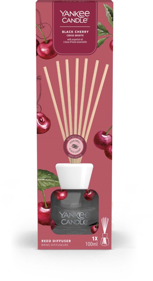 Een kersengeurige aroma diffuser in een roze doos met kersen en een witte fles, die geurstokken afgeeft.