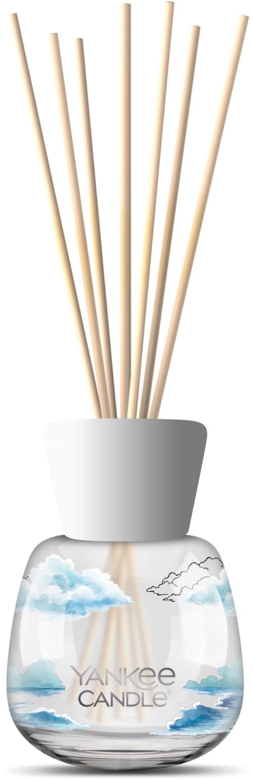 Een glazen waxinelichthouder met blauwe lucht en wolken, met houten doeltikkers voor een diffuser.