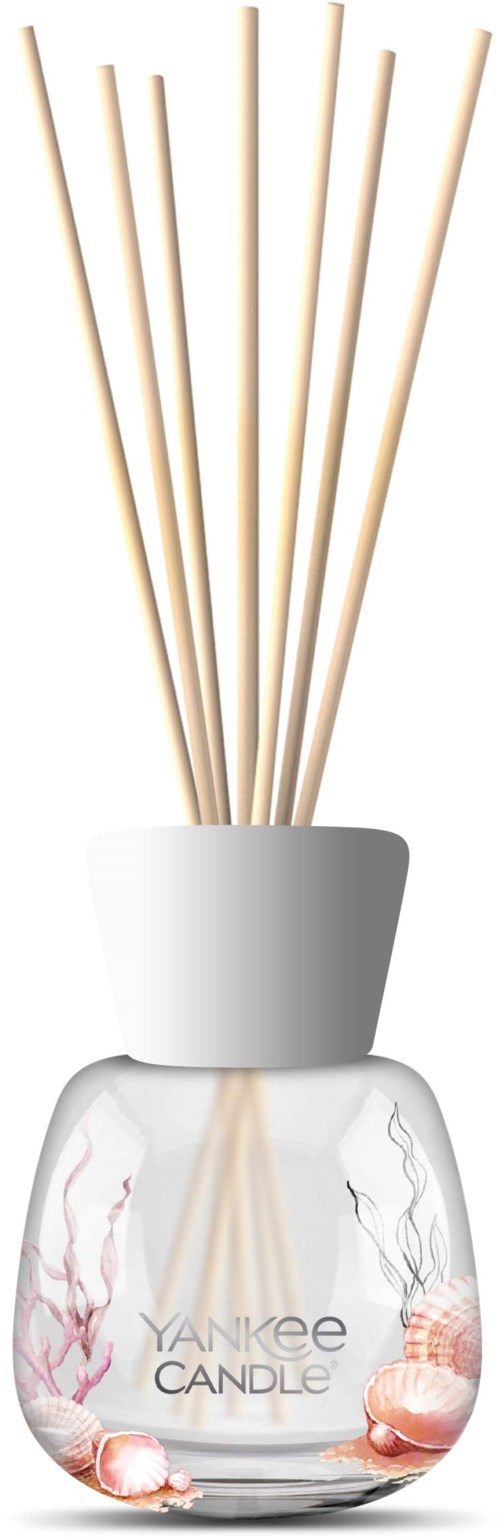 Een heldere glazen pot met witte deksel bevat acht dunne, beige rietjes. De pot heeft 'Yankee Candle' erop en is versierd met schelpen en koraal.