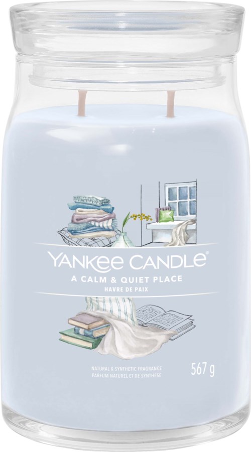En blå Yankee Candle-glasburk med en etikett som visar ett mysigt rum med böcker, ett fönster och en växt.