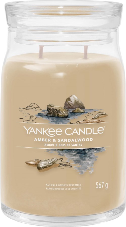 A candle in a glass jar with a sandy beige color, rocks, and water design, labeled Yankee Candle Amber & Sandalwood.