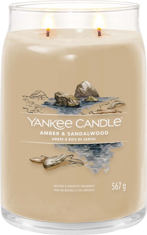 A candle in a glass jar with two wicks, labeled 'Yankee Candle Amber & Sandalwood,' with a beach scene illustration.