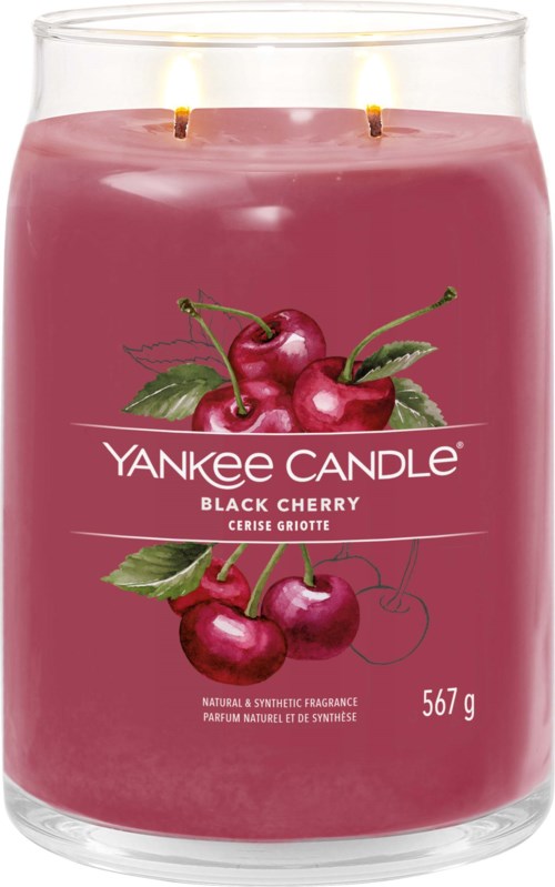 A large pink candle with cherries on the label, two flames on top, in a glass holder.