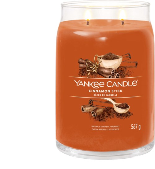 Een grote oranje kaars met twee brandende lonten en kaneel, vanille en specerijen op het etiket.