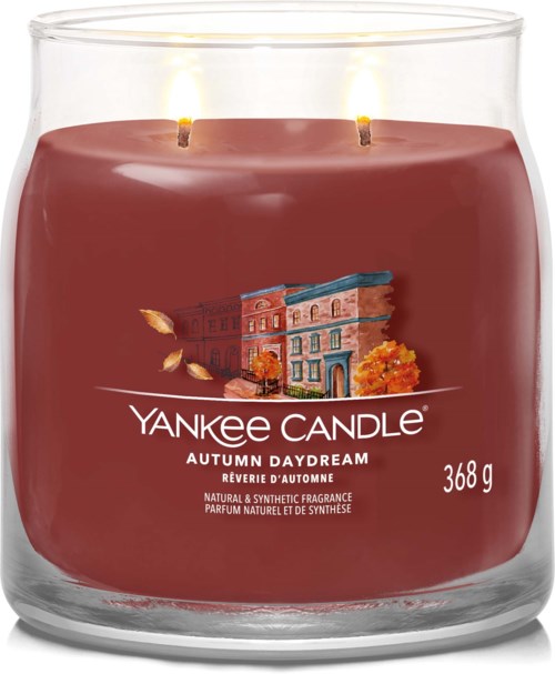 A red candle in a glass container with a cityscape illustration and two lit wicks.