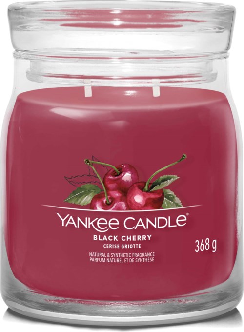 Een roze geurkaars in een glazen pot met kersen en groene bladeren op het label. Het is een Yankee Candle met kersengeur.