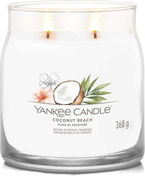 En vit ljuslykta med två tända vaxstickor, kokos- och blomsterdesign, etiketten säger Yankee Candle Coconut Beach, 368 g.
