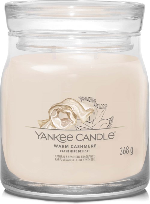 Een witte geurkaars in een glazen pot met label met een cashmere-rozenafbeelding en tekst 'Yankee Candle' en 'Warm Cashmere.'