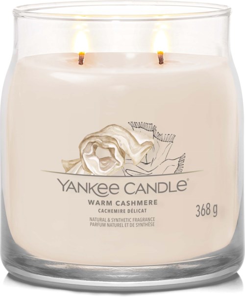 Een witte kaars in een doorzichtige glazen pot met twee brandende lonten, gelabeld 'Yankee Candle', geur is warm kasjmier.