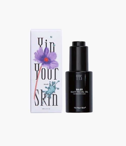 Mustavalkoinen kasvoöljypullo ja valkoinen laatikko, jossa on lilakukka ja teksti "Unlock Your Skin".
