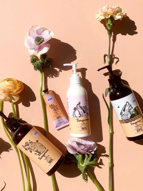 Drei Blumenstiele und drei Flaschen mit Etiketten, einige mit Pumps, sind auf einem rosa Hintergrund angeordnet.