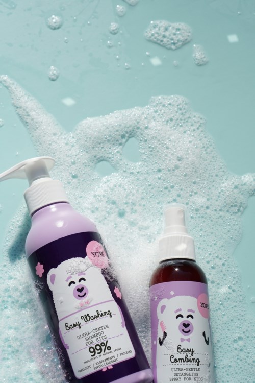 Kaksi vauvojen shampoopakkia, joissa on karhukuviot ja suppilonkannut, kelluvat saippuaisessa vedessä ja kuplissa.