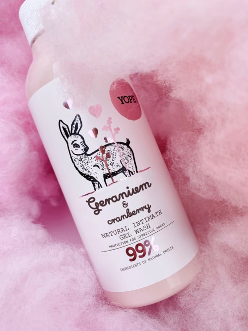 Valkoinen pullo kermavaahdon tuoksuiselle vartalopesulle, jossa on söpö poro-illustraatio ja pinkkejä sydämiä, makaa pinkillä jotkapeitteellä.