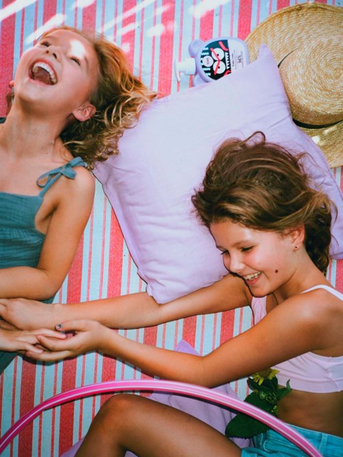 Zwei Frauen liegen auf einer bunten gestreiften Decke, halten Händchen, lachen und haben Spaß im Freien.