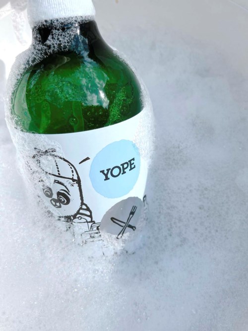 Eine grüne Flasche mit "YOPE"-Aufkleber liegt im Schaum mit Blasen.