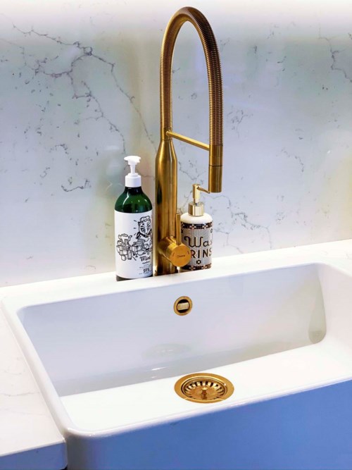 Ein weißes Waschbecken mit goldener Armatur und zwei Seifenspendern auf einer Marmorarbeitsplatte.