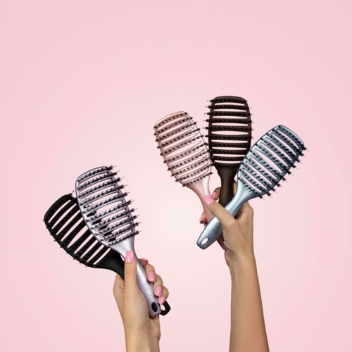 Four hairbrushes in black, pink, brown, and silver held by hands against a pink background.
