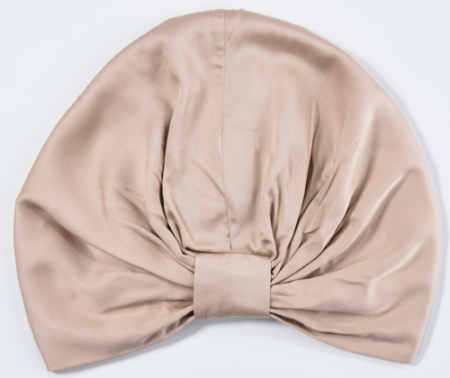 A beige satin headband with a large bow in the center and gathered fabric. Clean, soft-looking material.
