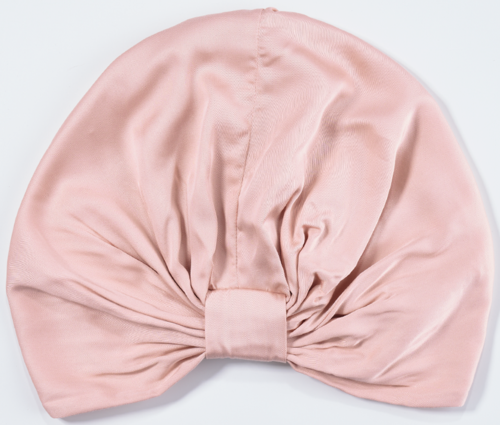 A soft pink fabric headscarf with a bow in the center, laid flat on a white surface.