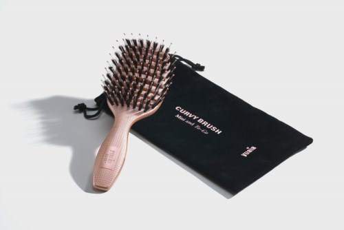 En trehårbørste med svarte børster og en svart pose merket "Curly Brush" ligger på en hvit overflate.