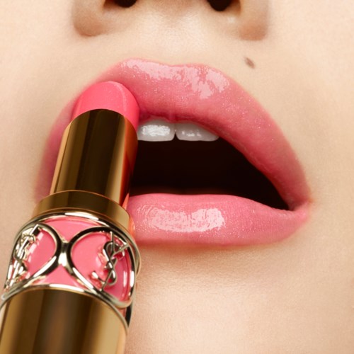 Närbild av läppar med rosa läppstift, öppen mun och en läppstiftstub nära läpparna.