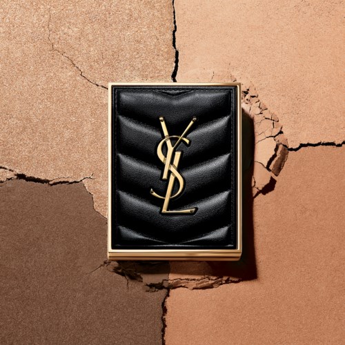 En svart läderbox med en guld YSL-logotyp, placerad på en sprucken beige väggyta.