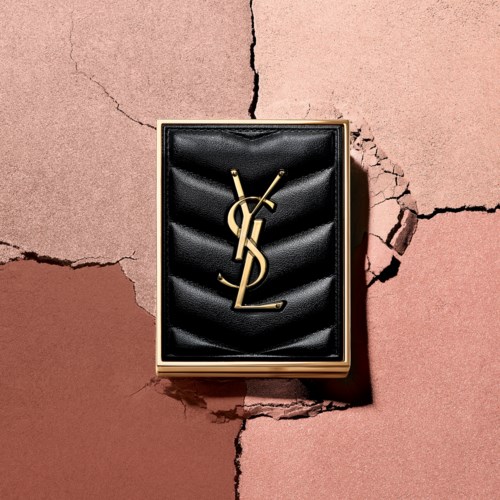 En Yves Saint Laurent-logotyp i ett svart sammetsfodral på en sprucken rosa och brunt väggbakgrund.