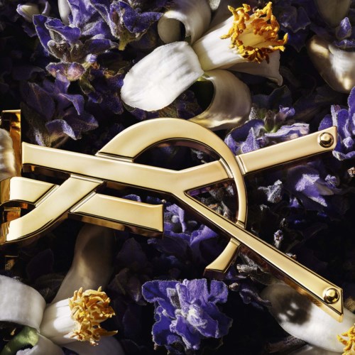 En skinnende gull YSL-logo omgitt av lilla blomster og hvite blomster med gult sentrum.