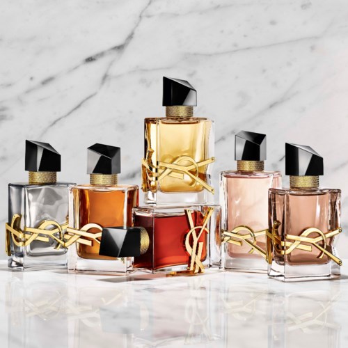 Zes parfumbus in verschillende kleuren met zwarte doppen en gouden decoraties, gerangschikt op een witte marmeren ondergrond.