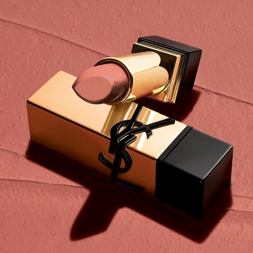 A lipstick tube with a black and gold design lies on a pink surface, casting a shadow.