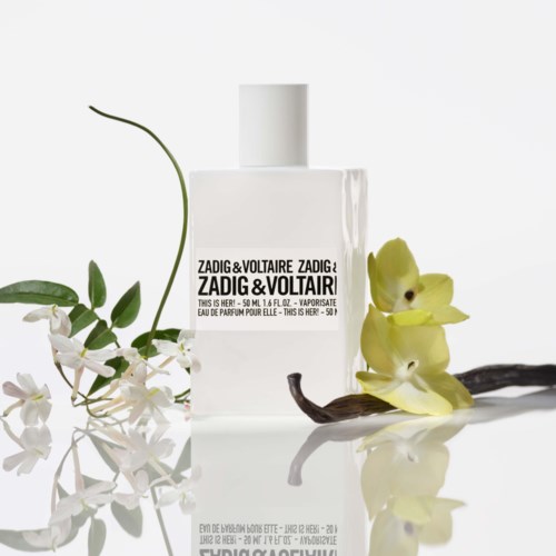 Eine weiße Parfüfflasche mit schwarzem Text neben gelben Blumen und grünen Blättern.