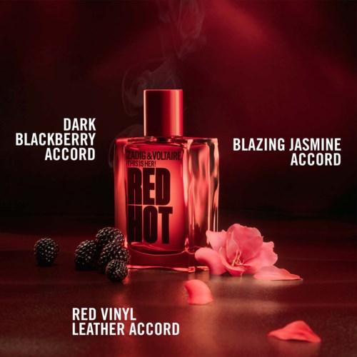 Red perfume bottle with blackberries, pink flower petals, and ashes around it on a dark background.