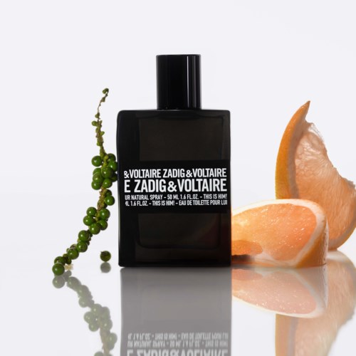Eine schwarze Parfüflasche mit grünen Beeren und Orangenstücken daneben.