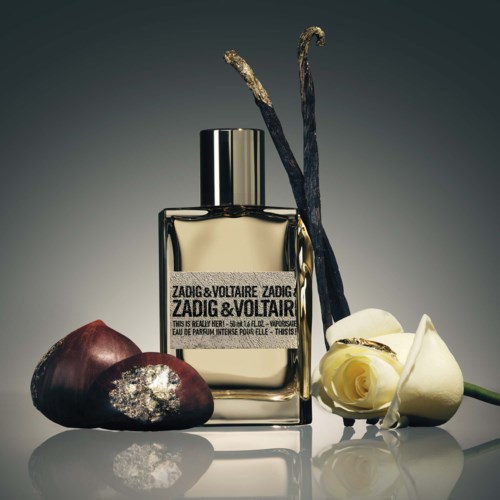 Eine Parfüfflasche mit Vanilleblumen und Vanilleschoten, dazu ein dunkler Stein und eine weiße Rose.