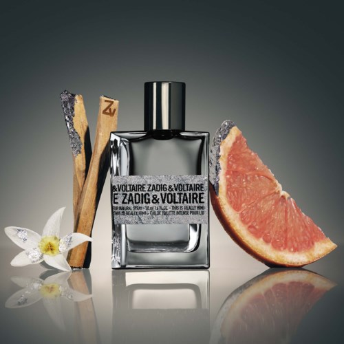 Ein Parfümflasche, umgeben von Zimtstangen, einer Orchideenblume und einer Grapefruit-Scheibe auf einer reflektierenden Oberfläche.