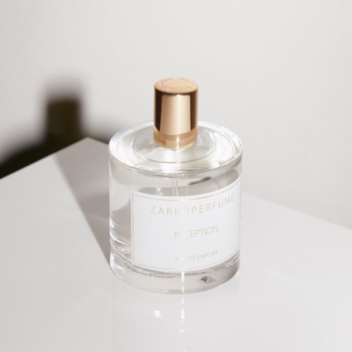 Läpinäkyvä hajuvesipullo kulttikannella valkoisella pinnalla; etiketti lukee 'ZARKOPERFUME INCEPTION' ja 'eau de parfum'.