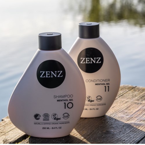 Two bottles of hair care products, shampoo and conditioner, with black caps, placed on a wooden surface near water.