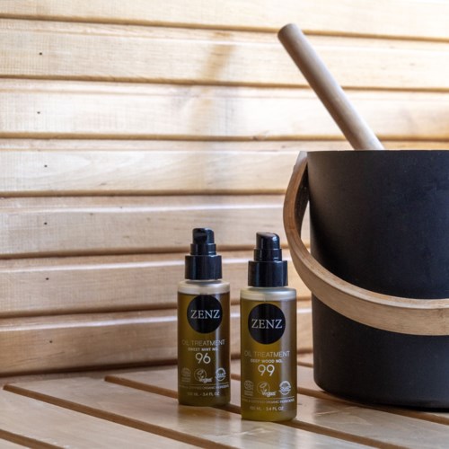 Two bottles labeled 'ZENZ' stand next to a black container with a stick inside, on wooden slats.