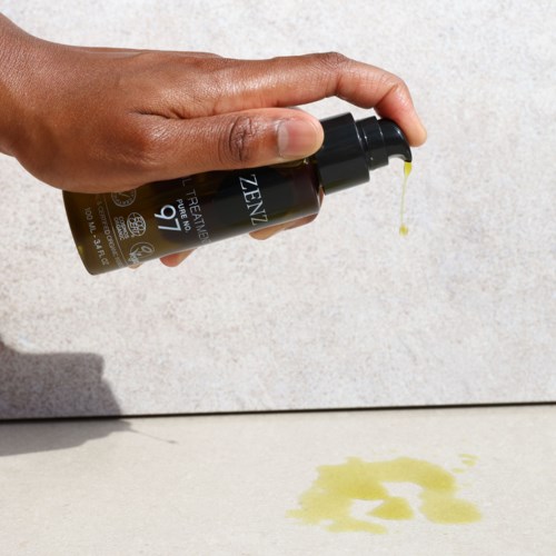 A hand is holding a dropper bottle, with some liquid falling onto the surface below.