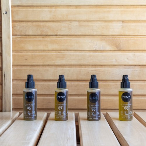 Four bottles of wellness treatment spray are lined up on a wooden surface against a wooden wall background.
