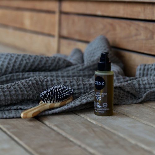 A hairbrush and a bottle of hair treatment product placed on a soft gray blanket.