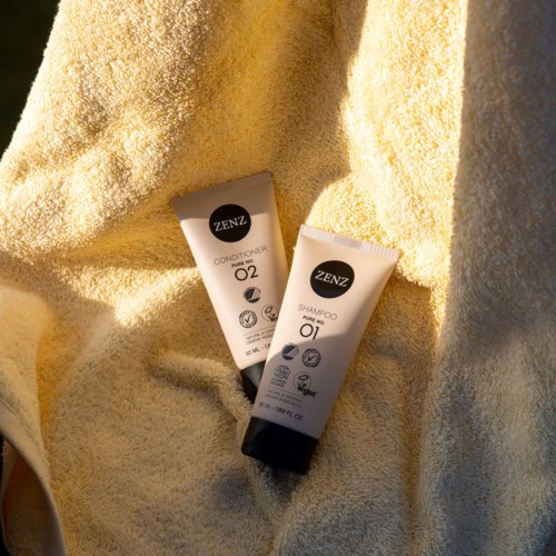 Two small tubes, one for conditioner and one for shampoo, placed on a soft yellow towel.