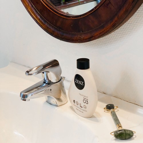 A bathroom sink with a silver tap, a bottle labeled ZENZ, and a green stone on a string.