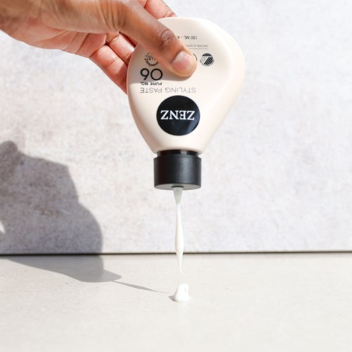 Hand squeezing a sizable white bottles of glue onto a surface.