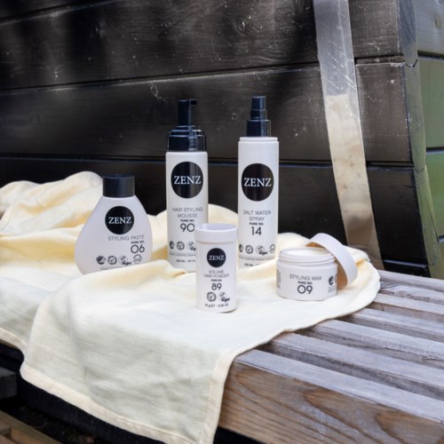 A set of hair styling products, including spray, mousse, salt water spray, and styling paste, arranged on a cloth on wood.