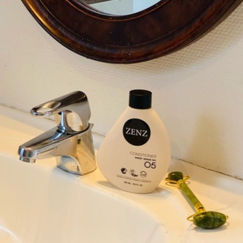 A soap dispenser labeled 'ZENZ', a yellow-green stone on a string, and a faucet on a bathroom sink.