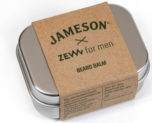 En metallburk med skäggbalsam, omsluten av en brunt pappersetikett med grön text och information.
