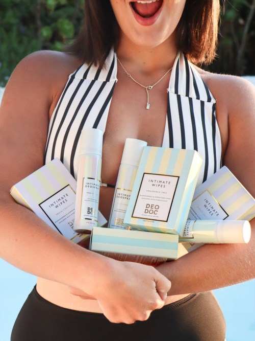 A woman wearing a striped top holding multiple skincare or cosmetic products and smiling.
